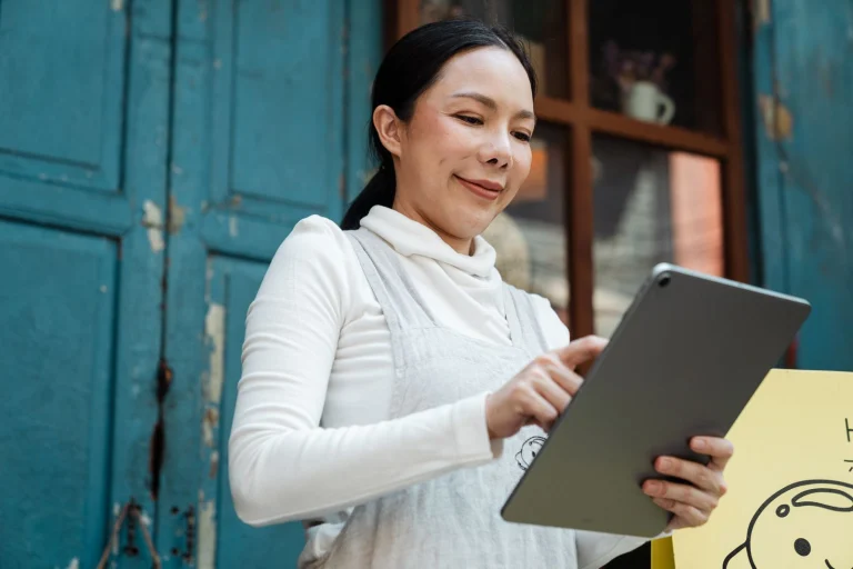 Une commerçante souriante consulte sa tablette devant sa boutique