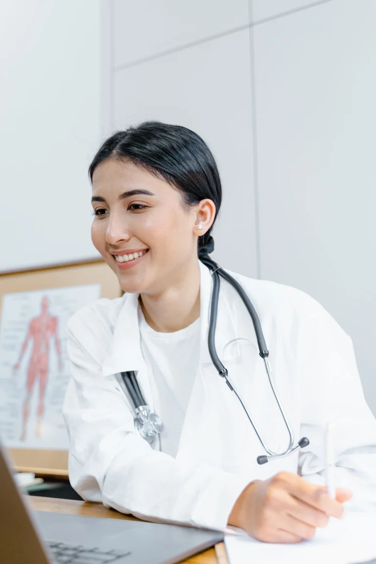 Une médecin souriante travaille sur son ordinateur dans son cabinet